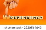 Small photo of Codependency or dependency symbol. Concept words Codependency and dependency on wooden cubes. Psychologist hand. Beautiful orange background. Psychological codependency dependency concept. Copy space.