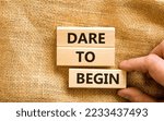 Small photo of Dare to begin symbol. Wooden blocks with words 'Dare to begin'. Beautiful canvas background, businessman hand. Business, dare to begin concept, copy space.