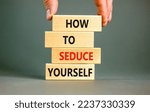 Small photo of How to seduce yourself symbol. Concept word How to seduce yourself on wooden blocks. Businessman hand. Beautiful grey table grey background. Business and how to seduce yourself concept. Copy space.