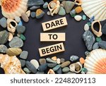 Small photo of Dare to begin symbol. Wooden blocks with words 'Dare to begin'. Beautiful black background, seashells and sea stones. Business, dare to begin concept, copy space.