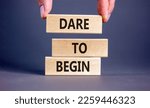 Small photo of Dare to begin symbol. Wooden blocks with words 'Dare to begin'. Beautiful grey background, businessman hand. Business, dare to begin concept, copy space.
