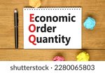 Small photo of EOQ economic order quantity symbol. Concept words EOQ economic order quantity on white note on beautiful wooden table wooden background. Pen. Business EOQ economic order quantity concept. Copy space.