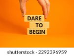 Small photo of Dare to begin symbol. Wooden blocks with words 'Dare to begin'. Beautiful orange background, businessman hand. Business, dare to begin concept, copy space.