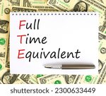Small photo of FTE Full time equivalent symbol. Concept words FTE Full time equivalent on white note. Dollar bills. Beautiful background from dollar bills. Business and FTE Full time equivalent concept. Copy space.