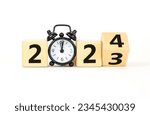 Small photo of Business concept of 2024 new year symbol. Businessman turns a wooden cube and changes number 2023 to 2024. Black alarm clock. Beautiful white background, copy space. 2024 happy new year concept.