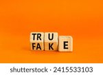 Small photo of Fake or true symbol. Turned wooden cubes and changed the word fake to true or vice versa. Beautiful orange table, orange background, copy space. Business and fake or true concept.