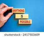 Small photo of Anything is possible symbol. Concept words Anything is possible on beautiful wooden blocks. Beautiful blue table blue background. Businessman hand. Business anything possible concept. Copy space.