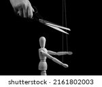 Small photo of Hand cutting strings over puppet with scissors. Freedom, overcoming addiction, liberation from slavery, abuse, abusive, toxic relationship cessation concept. Black and white. High quality photo