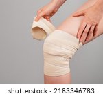 Small photo of Woman wrapping elastic bandage around painful knee to relieve pain or prevent injury. Sprained ligaments, meniscus tear, tendinitis. Leg trauma. Health care concept. High quality photo