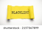 Small photo of Word Blacklist on white background through hole in yellow paper, top view