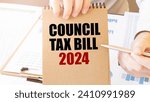 Small photo of Text COUNCIL TAX BILL 2024 on brown paper notepad in businessman hands on the table with diagram. Business concept