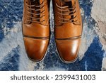 Small photo of A pair of premium calfskin boots on a blue background. Horizontal shot.