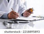 Small photo of male medicine doctor hand holds the bottle of pills and writes a prescription to the patient at the worktable. Panacea and life save, prescribing treatment legal drug store concept.