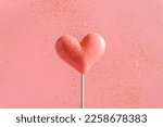 Pink Valentine's day heart shape lollipop candy on empty pastel pink background with golden flying sequins. Love Concept. Minimalism colorful style