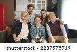 Small photo of Young couple with children, their son and elderly parents sitting on sofa in living room, taking self portraits together. Portrait of happy cheerful big family smiling at camera in cozy living room.