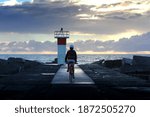 Silhouette of a person riding a bike along a rocky coastline with a lighthouse.