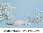 A minimalistic scene of a lying stone with flowers on a light blue background. Catwalk for the presentation of products and cosmetics. Showcase with a stage for natural products.