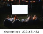 family mother, father and children watch a projector, movies with popcorn in the evening in the courtyard
