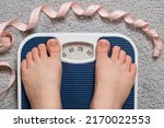 Small photo of Women's bare feet on floor scales and measuring tape, weight 60-70 kilograms, top view. The idea of obesity, weight loss and excess weight.