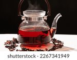 Red hibiscus tea from the petals of a Sudanese rose in a glass teapot, steam from a teapot on a black background