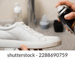 Small photo of Applying a water-repellent hydrophobic spray to white women's sneakers. Protection of shoes from moisture, dirt and unpleasant odor.