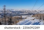 Small photo of The cabs of the funicular move along the ropes over the snow-covered valley. Bare trees and firs are visible below. A picturesque mountain range in the distance. Altai. Manzherok Ski Resort