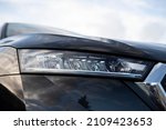 Angled view on headlight of new black car model with basic LED and bulbs version, visible glossy chrome grille frame