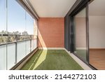 Terrace with glass wall, artificial grass floor and painted iron railing in urban residential house on a sunny spring day