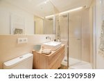 Small photo of Bathroom with wooden vanity with frameless mirror along the wall shower stall with glass partition and white porcelain sink