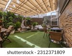 Small photo of Terrace of a house with artificial grass floors, tables, outdoor seating, lots of plants and an extended retractable awning
