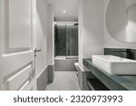 Small photo of a modern design bathroom with a bathtub with a tempered glass screen, green tiles, porcelain sinks, a circular mirror, white carpentry, black details and gray terrazzo floors