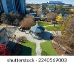 an aerial shot of a round blue and white pergola at the Decatur Square surrounded by red and yellow autumn trees, lush green trees and grass, office buildings and people with a clear blue sky 