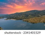 aerial shot of the rippling blue waters of Silverwood Lake with a beach, mountains covered in lush green trees, plants and grass, powerful clouds at sunset in Hesperia California USA
