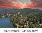 Small photo of aerial shot of a gorgeous summer landscape with rippling lake water, lush green trees, grass and plants with homes on the hillside, powerful clouds at sunset at Lake Gregory in Crestline California