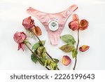 Small photo of Pink dried rose, alarm clock and woman underwear. Concept of menopause, withered female beauty and the cessation of monthly menstrual cycles. World menopause day