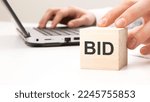 Small photo of man holding wooden cube witt letters BID in the background a laptop on a white office table background