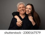 Small photo of Studio portrait of a Ukrianian father in his 60s and his adult daughter in her late 20s. They are both wearing black and the daughter is hugging her father. The background is grey.
