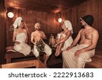 Russian bathhouse. Two couple relaxing and sweating in wooden sauna with hot steam. Four person with bath besoms resting on bench in spa complex. Wellness, self care, healthy concept. Copy text space