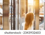Rear view of blonde girl kid finger pressing button to call elevator in modern residential building. Human child hand pushing buttons of glass lift call, sunshine. Up to high floor. Copy ad text space