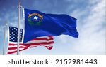 The Nevada state flag waving along with the national flag of the United States of America. In the background there is a clear sky. Nevada is a state in the Western region of the United States