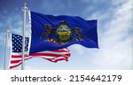 The Pennsylvania state flag waving along with the national flag of the United States of America. In the background there is a clear sky. Pennsylvania is a U.S. state in the northeast