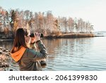 Small photo of Young woman looking through binoculars at birds on the lake. Birdwatching, zoology, ecology. Research in nature, observation of animals Ornithology autumn bird migration selective focus