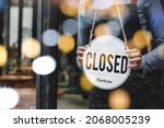 asian waitress staff woman wearing apron turning CLOSED sign board on glass door with bokeh light in modern cafe coffee shop, cafe restaurant, retail store, small business, food and drink concept