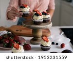 Cooked muffins are displayed on special stand. Small, chocolate brownies decorated by cream, strawberries and blueberries. Delicious dessert cupcake make by young girl with special recipe