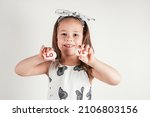 Small photo of Smiling little girl in white clothes hold two white smooth stones with syllables lo and ve painted red on white background. Family, love, birthday, Valentine's day, Mother's day concept. Copy space.