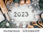 Small photo of Numbers 2023 written on flour sprinkled on black table with branches of Christmas tree, baking accessories and ingredients. Merry Christmas and Happy New Year 2023. Top view