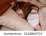 Small photo of A young girl is fast asleep lying on her stomach with her face in a pillow down in bed at home