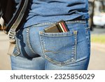Small photo of leather wallet with bank cards sticks out of the back pocket of jeans. The woman put her purse in the back pocket of her jeans. The concept of pickpocketing, indiscretion, frivolity.