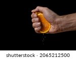 Hand squeezes juice from an orange on a black background. Fresh and juicy orange