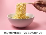 Boiled instant noodles on a pink background. Hand takes noodles with chopsticks for food. Fast food. Modern food.